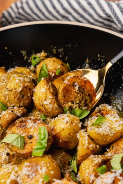 Black bowl with roasted pesto potato salad sprinkled with parmesan cheese and fresh basil.