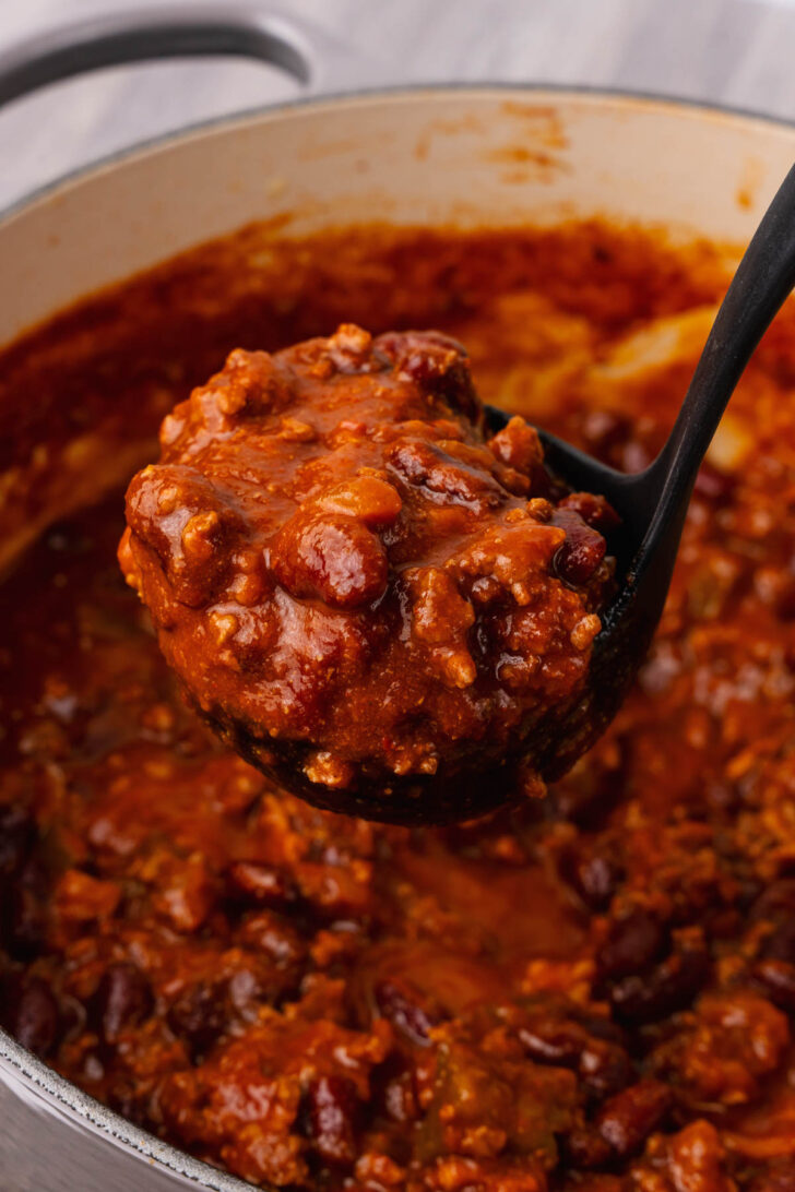 Black ladle with ground beef and bean chili.