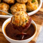 Cream cheese sausage ball on a metal skewer dipped into warm BBQ sauce in a small white bowl.