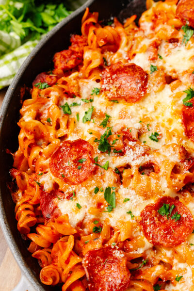 Baked pizza pasta casserole with melted mozzarella cheese and slices of pepperoni then topped with chopped green parsley.