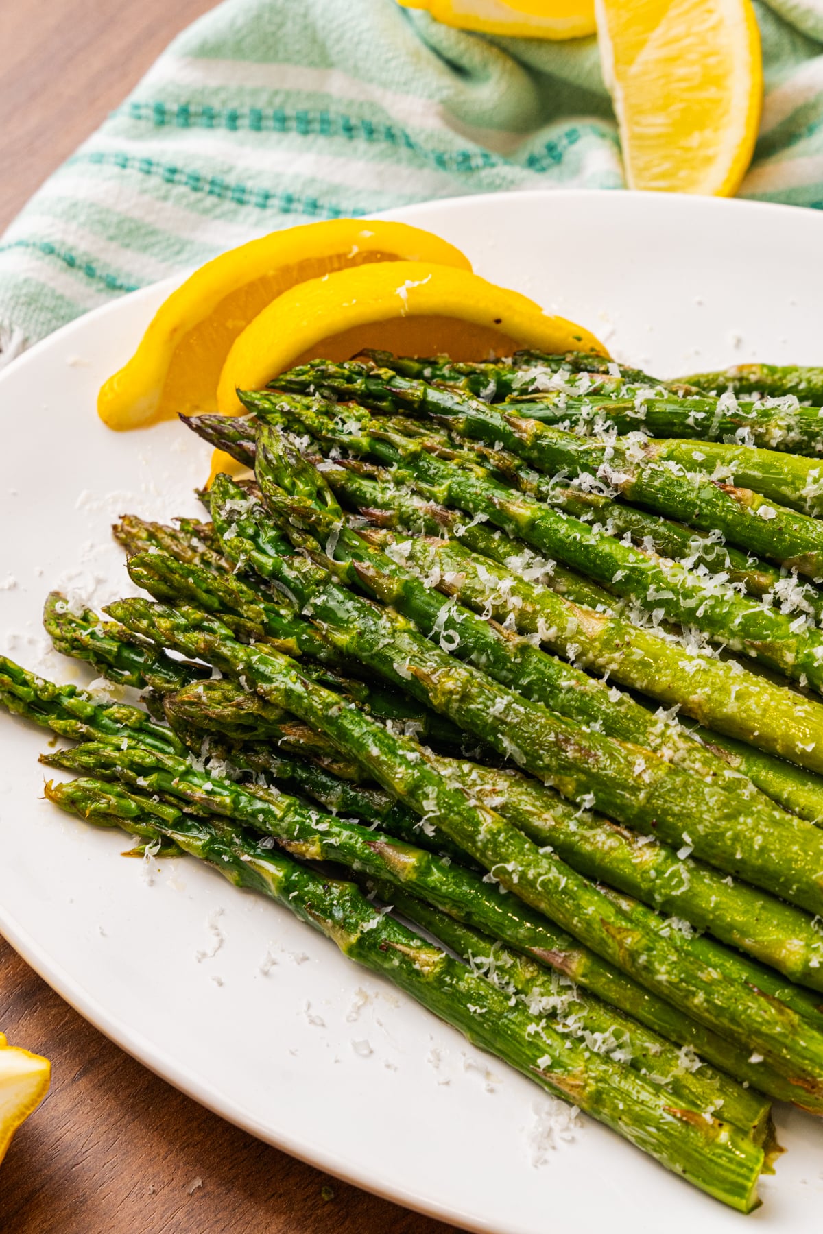 Roasted asparagus topped with grated Parmesan cheese and lemon on a white plated.