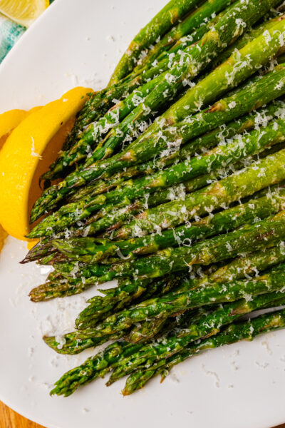 Roasted asparagus topped with grated Parmesan cheese and lemon on a white plated.