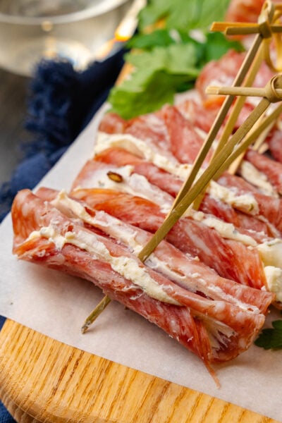 Wooden cutting board with cream cheese filled salami slices with a wooden pick.