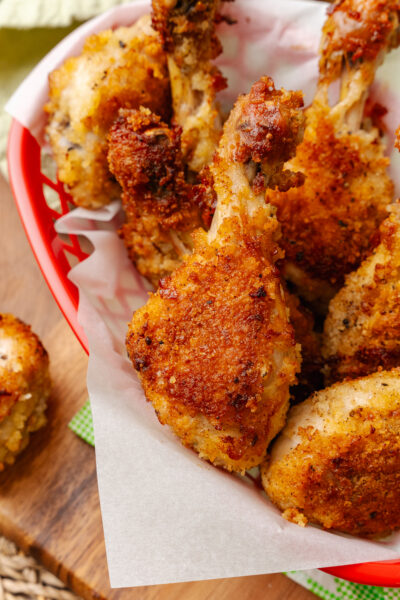 Fried chicken leg served on white parchment paper in a red basket.