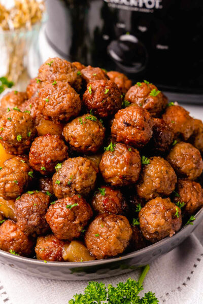 Cooked meatballs with pineapple chunks in a bowl served with wooden skewers.