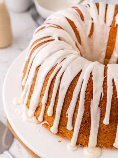 Eggnog pound cake with white icing drizzled, served on a white cake stand.
