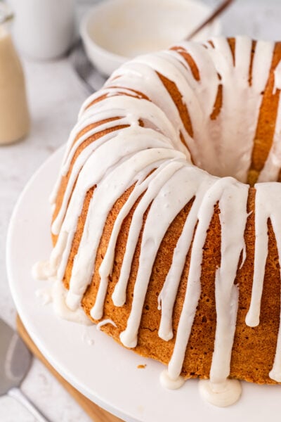 Eggnog pound cake with white icing drizzled, served on a white cake stand.