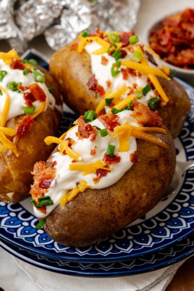Baked potatoes topped with sour cream cheese bacon bits and chives ontop of a nice blue plate.