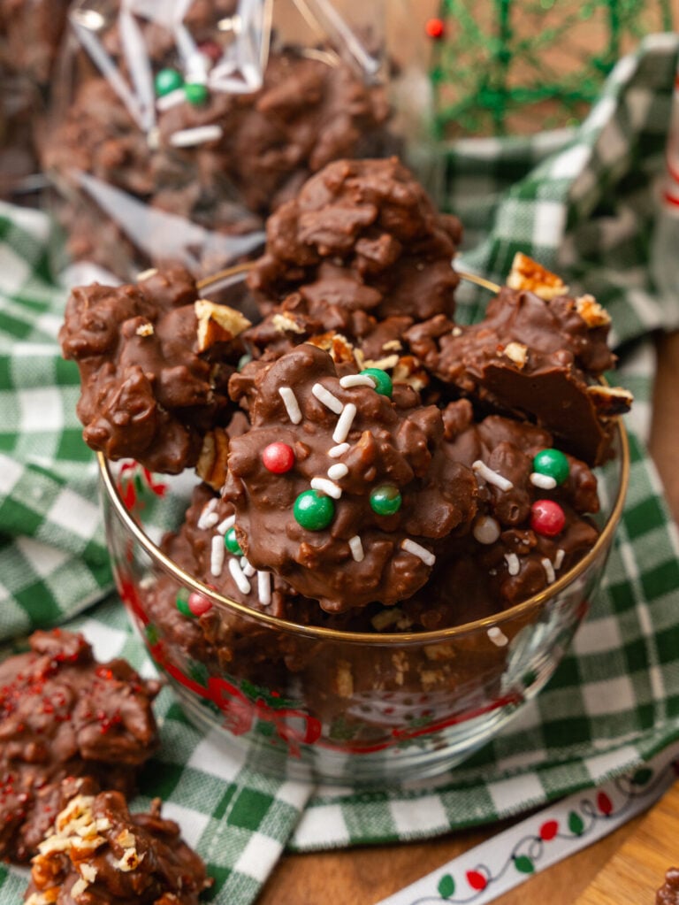 Chocolate pecan candy with green and red candy and white sprinkles and chopped pecans in a glass Christmas bowl.