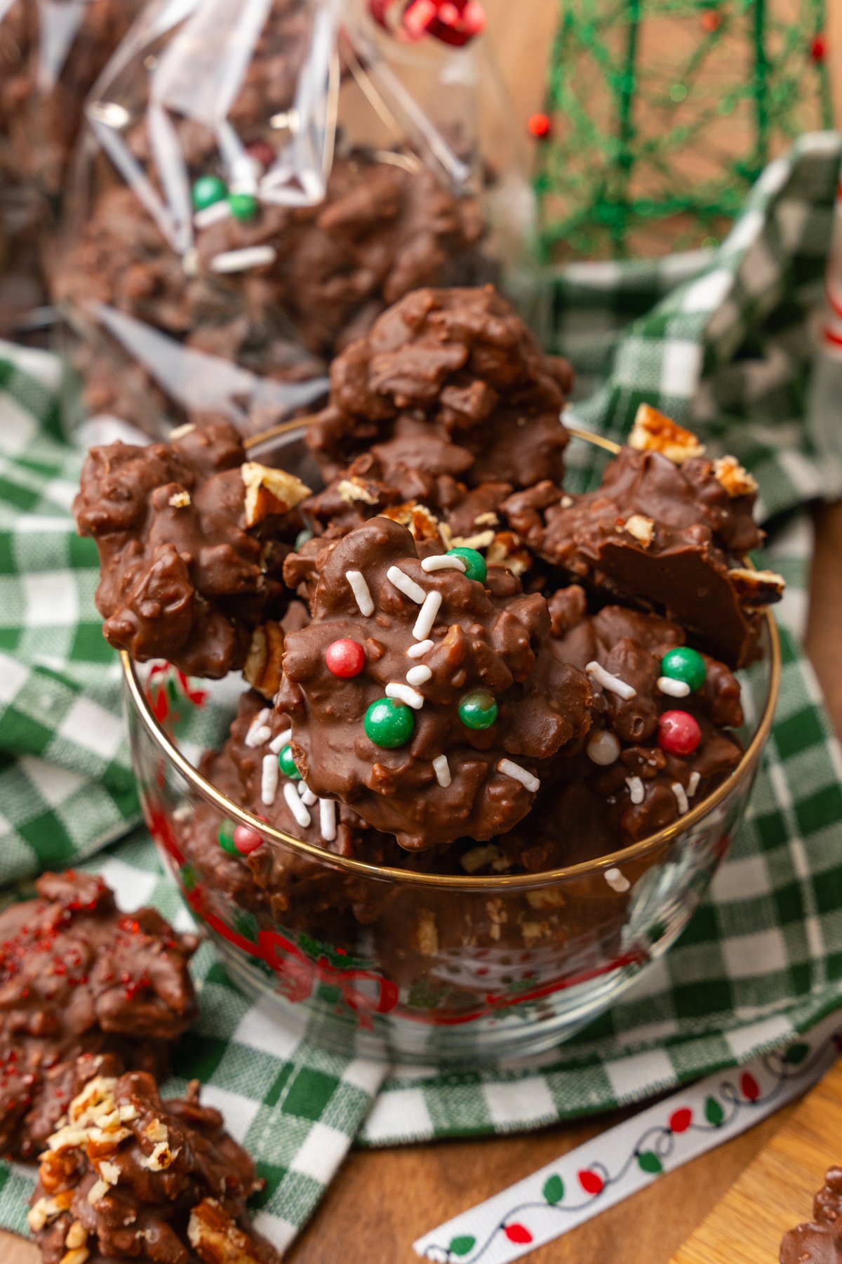 Chocolate pecan candy with green and red candy and white sprinkles and chopped pecans in a glass Christmas bowl.