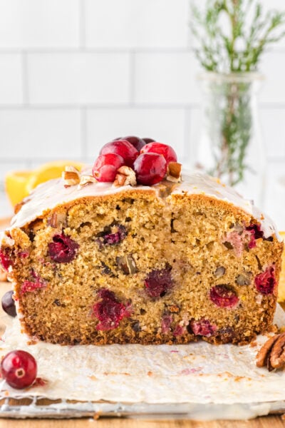 Slice of cranberry orange quick bread with pecans on a metal cooling rack, topped with fresh cranberries.