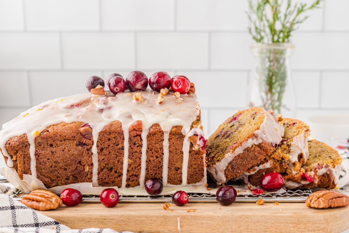Loaf of cranberry orange quick bread sliced and resting on a metal cooling rack topped with fresh cranberries and chopped pecans.