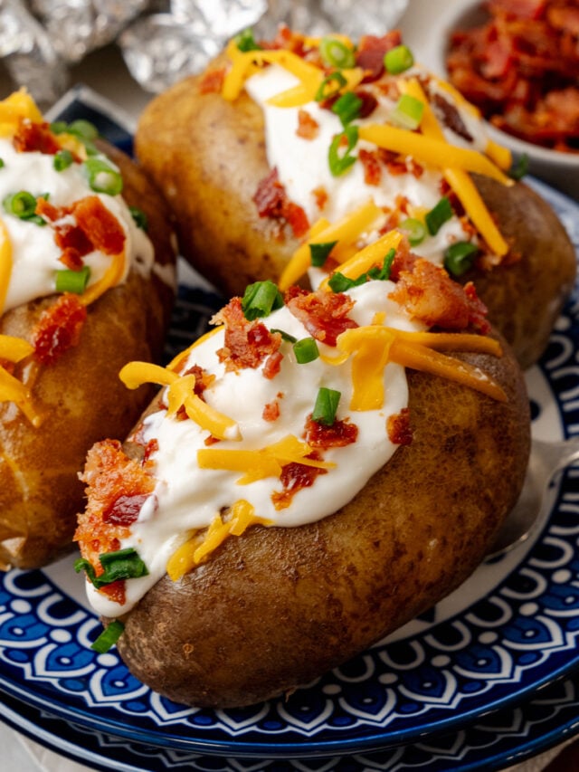 Baked potatoes topped with sour cream cheese bacon bits and chives ontop of a nice blue plate.