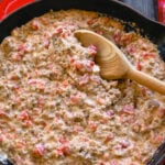Delicious sausage dip in a cast iron pan with bright red tomatoes and melted cream cheese and tortilla chips on the side ready for dipping.