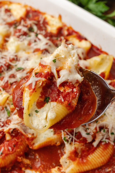 Spoon full of stuffed shells, stuffed with cheese parsley and marinara sauce inside a baking dish.