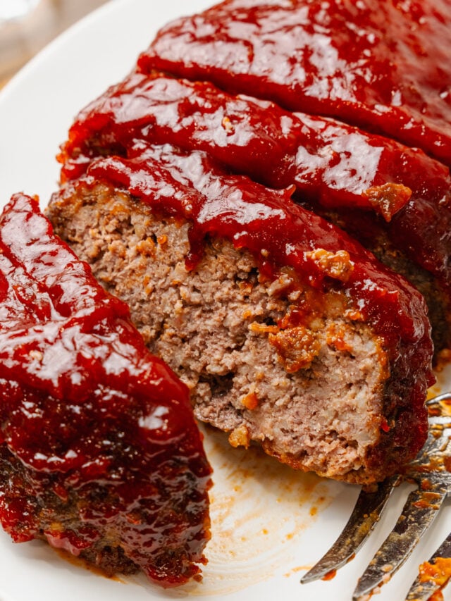 Sliced homemade meatloaf with thick glaze served on a white plate.
