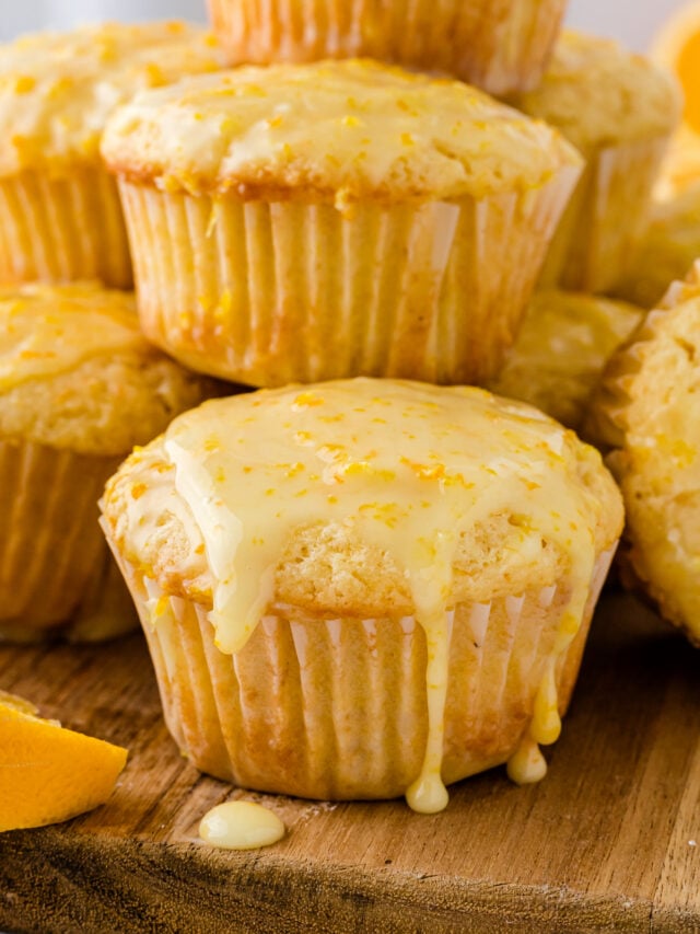 Glazed orange muffins stacked on top of each other on a cutting board.