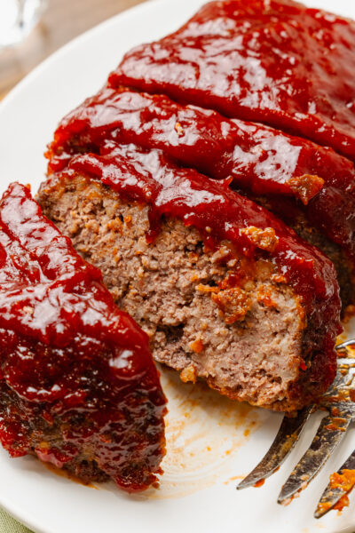 Sliced homemade meatloaf with thick glaze served on a white plate.
