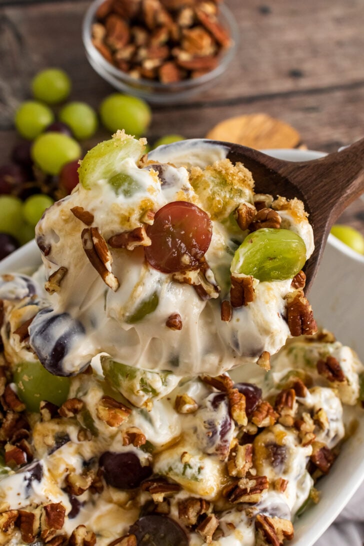 Grape Salad with chopped pecans in a white bowl with wooden spoon.