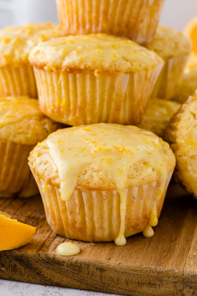 Glazed orange muffins stacked on top of each other on a cutting board.