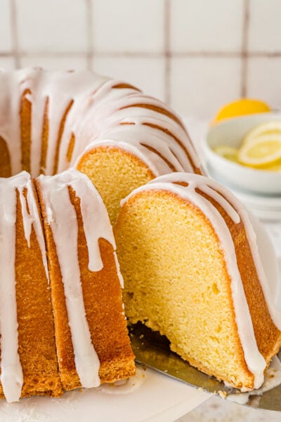 Slice of lemon pound cake being taken out with a nice drizzle of lemon icing on top of it.
