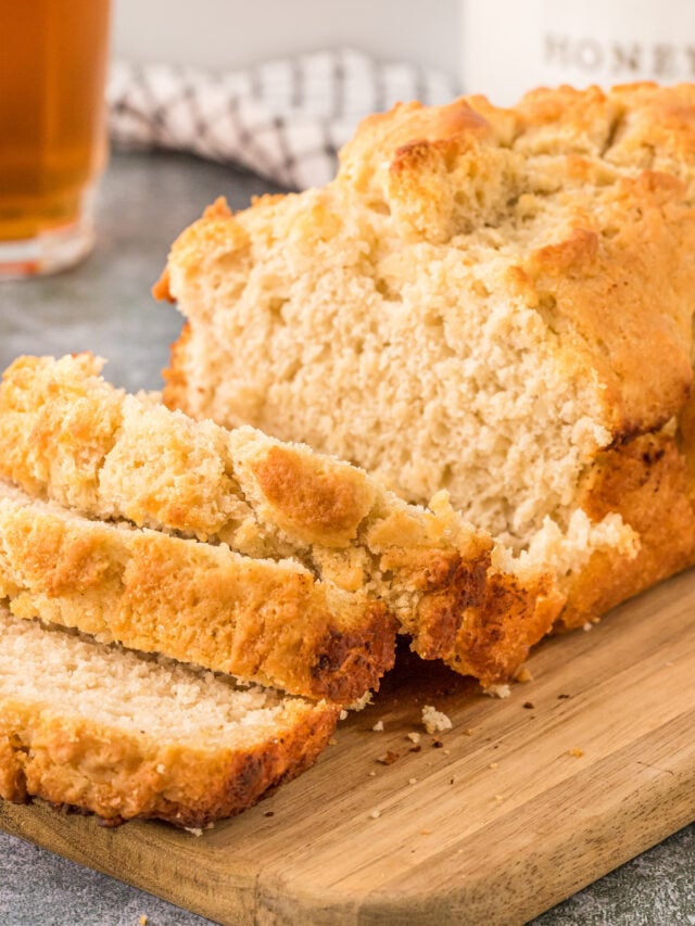 Beer bread sliced perfectly sitting on a wooden cutting board.