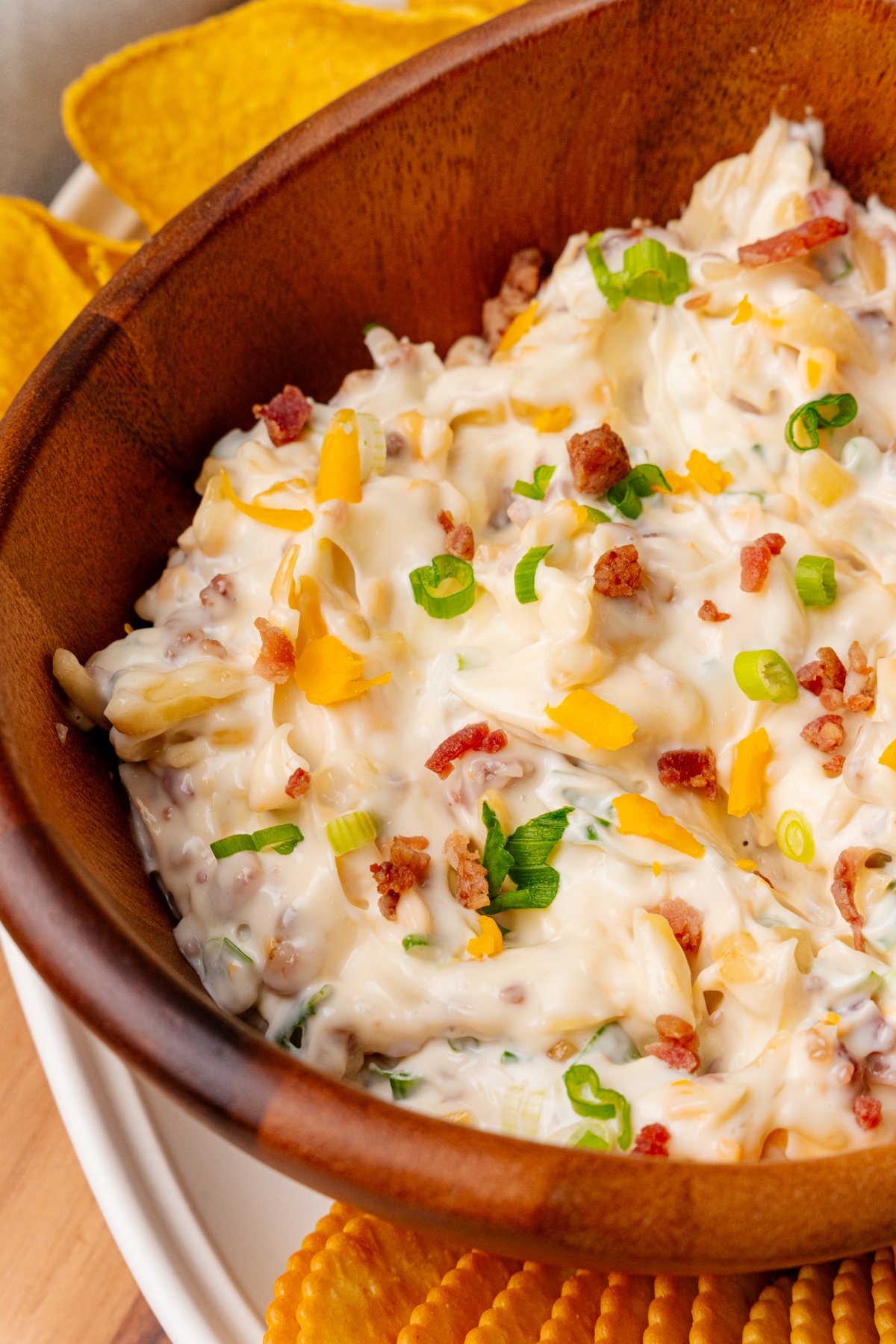 Shredded cheddar cheese green onion and candied bacon all showing on top of a freshly made million dollar dip all put inside a nice wooden serving bowl.