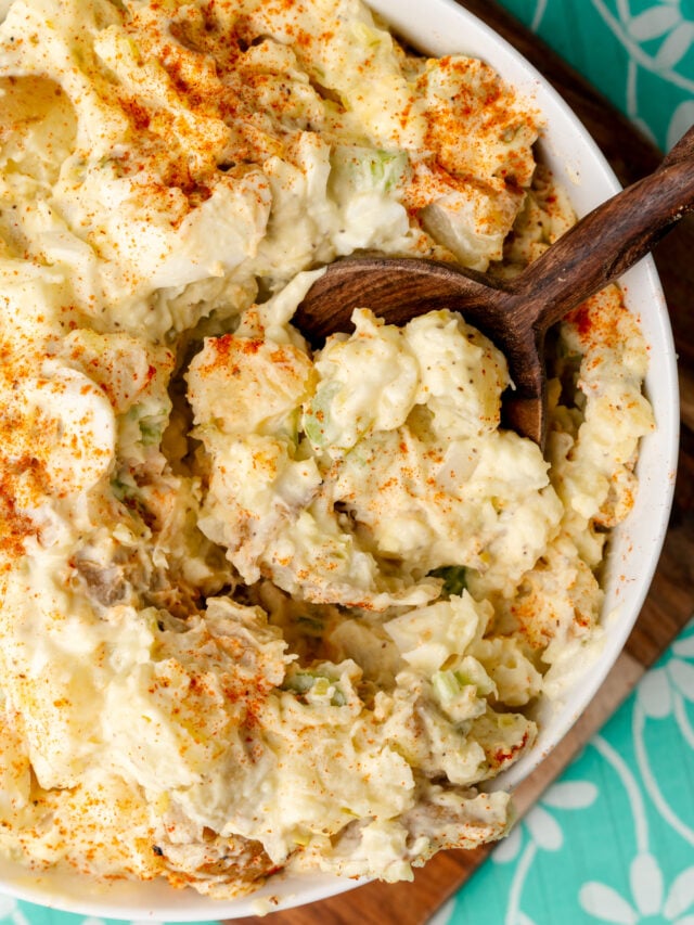Potato salad scooped out of a bowl with a wooden spoon.