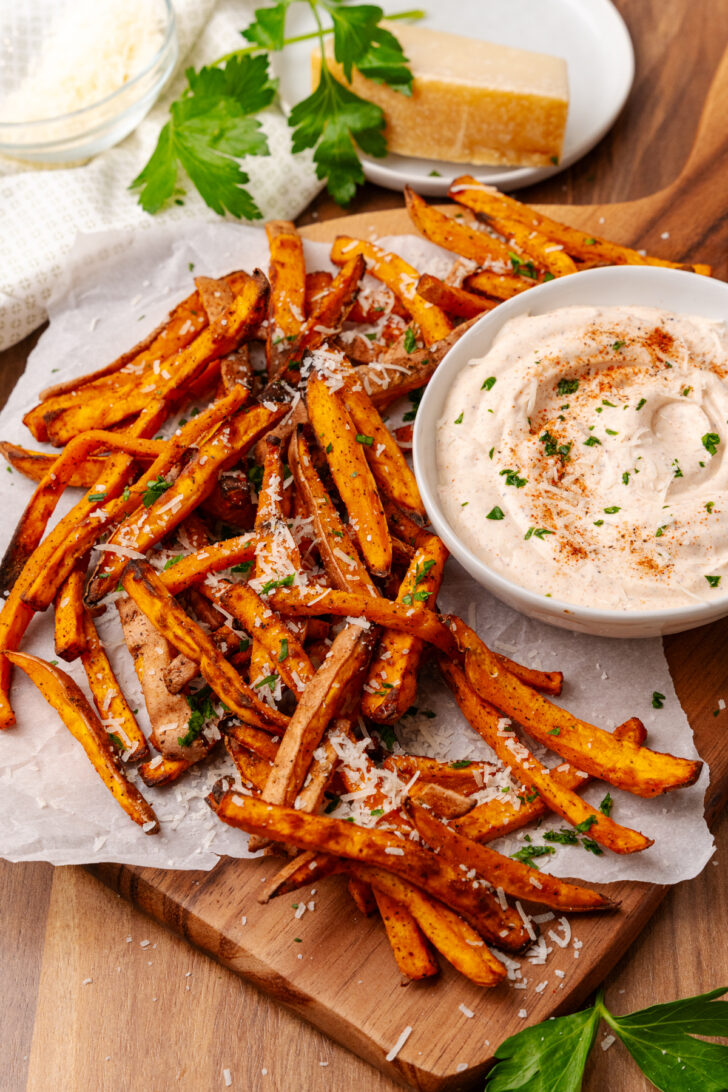 Crispy baked sweet potato fries topped with sea salt and fresh parsley, served with creamy dipping sauce on wooden board