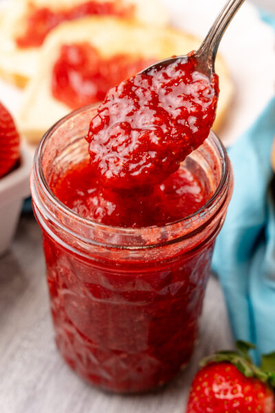 Easy strawberry jam in a glass jar served with a silvere spoon.