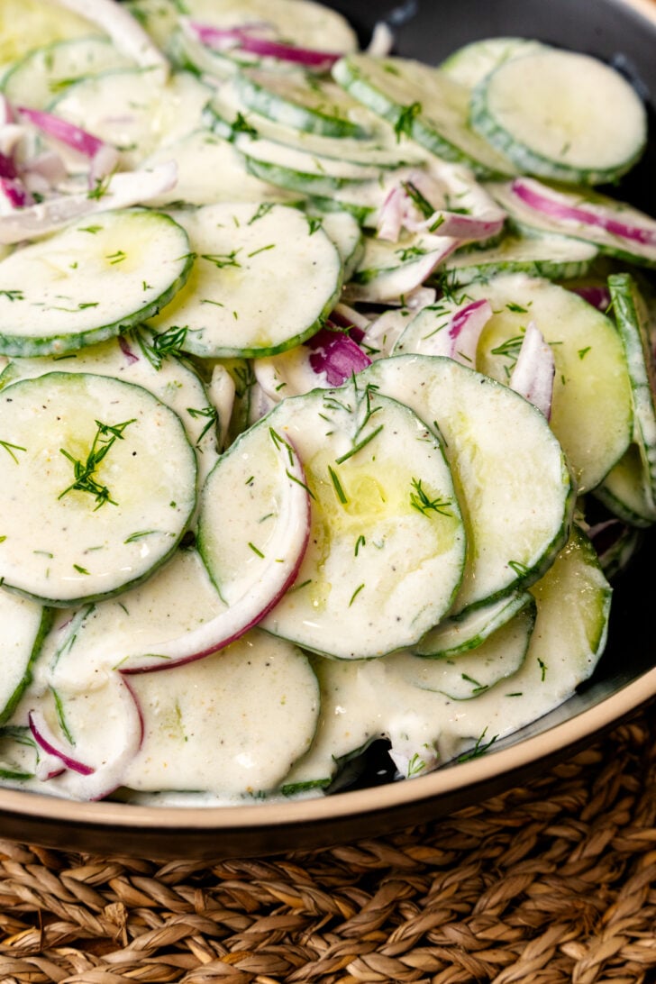 Creamy cucumber salad 6 with sliced cucumbers, red onions, and fresh dill in a white bowl on a woven placemat
