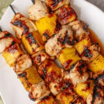 Hawaiian skewers featured on white plate with grilled chicken and pineapple chunks on metal skewers, charred edges visible