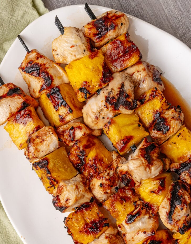 Hawaiian skewers featured on white plate with grilled chicken and pineapple chunks on metal skewers, charred edges visible