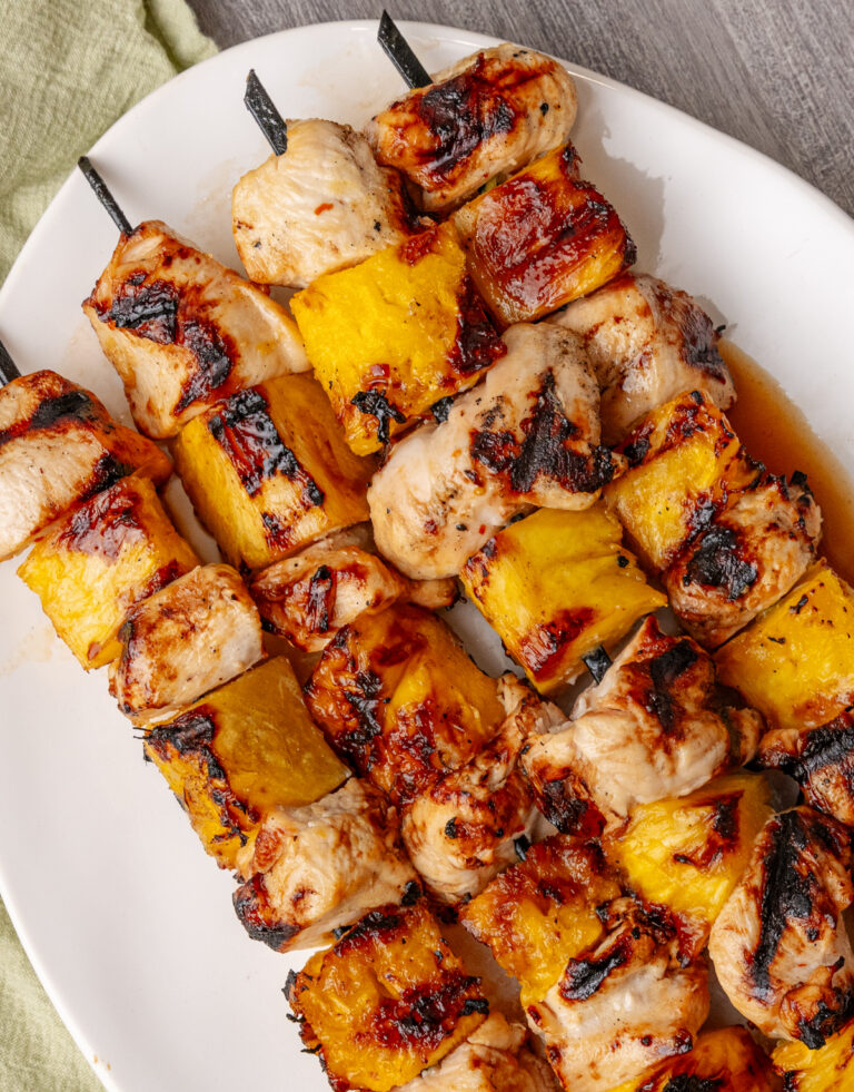 Hawaiian skewers featured on white plate with grilled chicken and pineapple chunks on metal skewers, charred edges visible