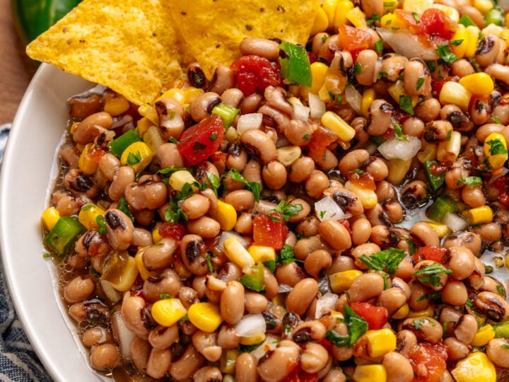 Southern caviar 6 bean dip in white bowl with tortilla chips, corn, peppers, and cilantro garnish, wooden surface