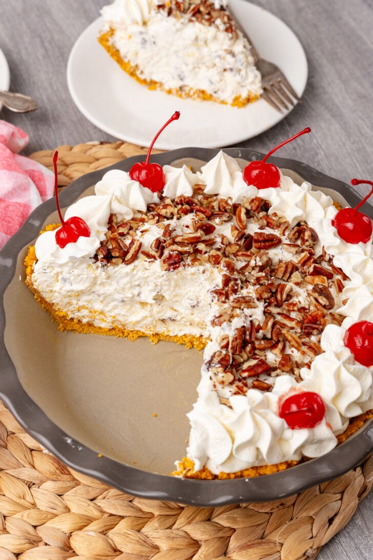 Million Dollar Pie with pecan topping, whipped cream piped border, and maraschino cherries on gray plate