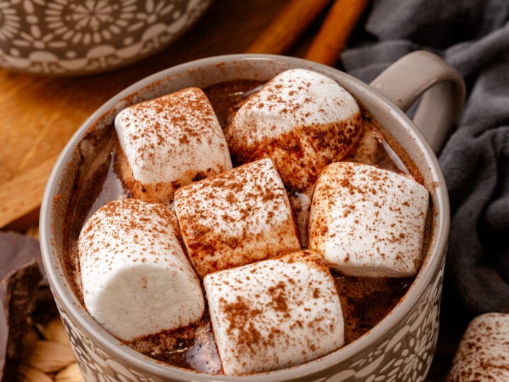 Easy Mexican Hot Chocolate mug topped with cinnamon-dusted marshmallows, served in decorative ceramic cup with cinnamon sticks and almonds
