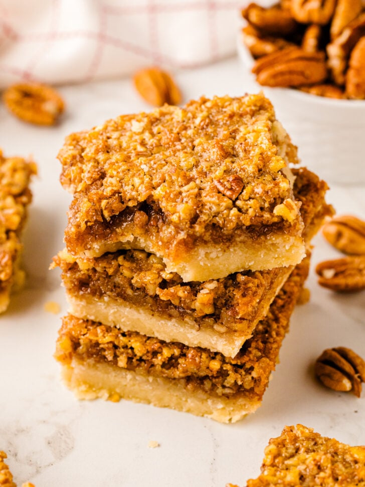 Southern Style Pecan Pie Bars stacked on white surface with pecans scattered around, overhead shot