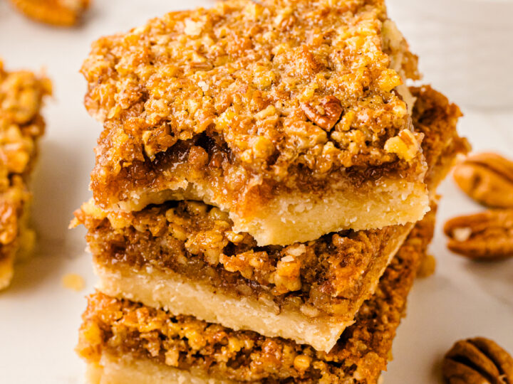 Stack of Southern Style Pecan Pie Bars with golden crumbly pecan topping and buttery shortbread base on white surface
