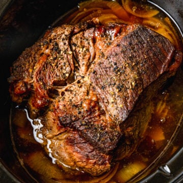 Slow cooker beef roast with caramelized onions and rich brown gravy in a black crockpot, overhead view
