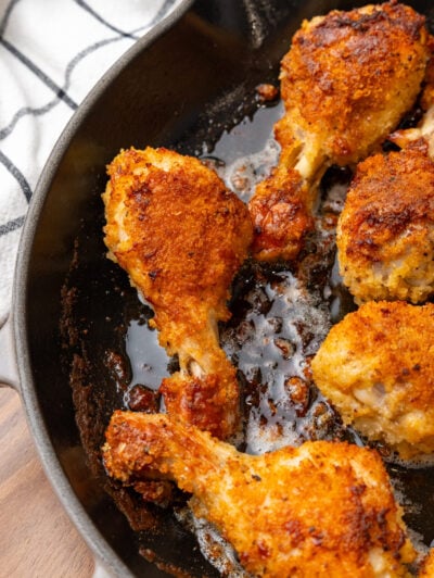 Golden oven fried chicken pieces sizzling in a cast iron skillet with crispy, seasoned coating and pan drippings