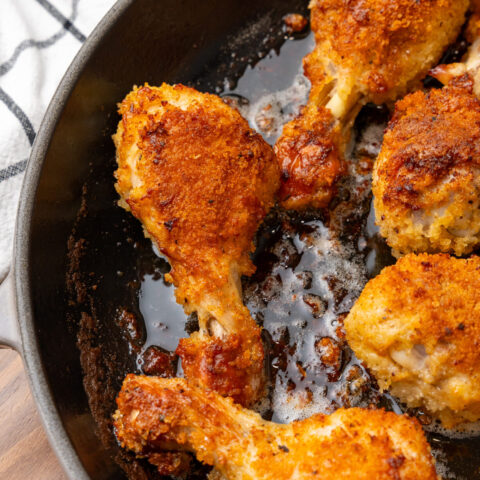 Golden oven fried chicken pieces sizzling in a cast iron skillet with crispy, seasoned coating and pan drippings