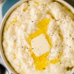 Crock Pot Southern Style Grits in white bowl with butter and black pepper garnish, overhead view