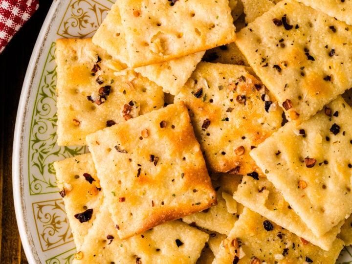 Homemade fire crackers 8 arranged on decorative plate with gold trim, topped with red pepper flakes and black seasoning, overhead view on wo