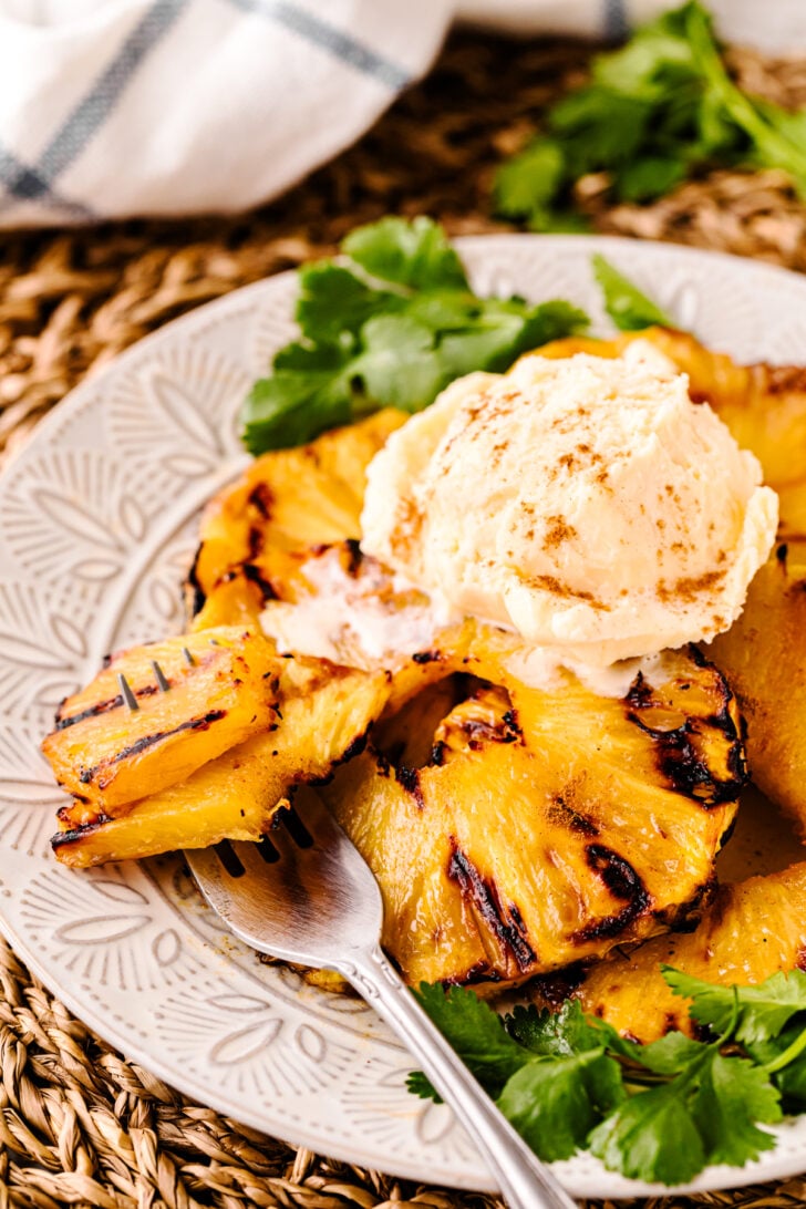 Grilled Pineapple with Brown Sugar Butter Glaze topped with vanilla ice cream and cinnamon, garnished with fresh cilantro on a decorative pl