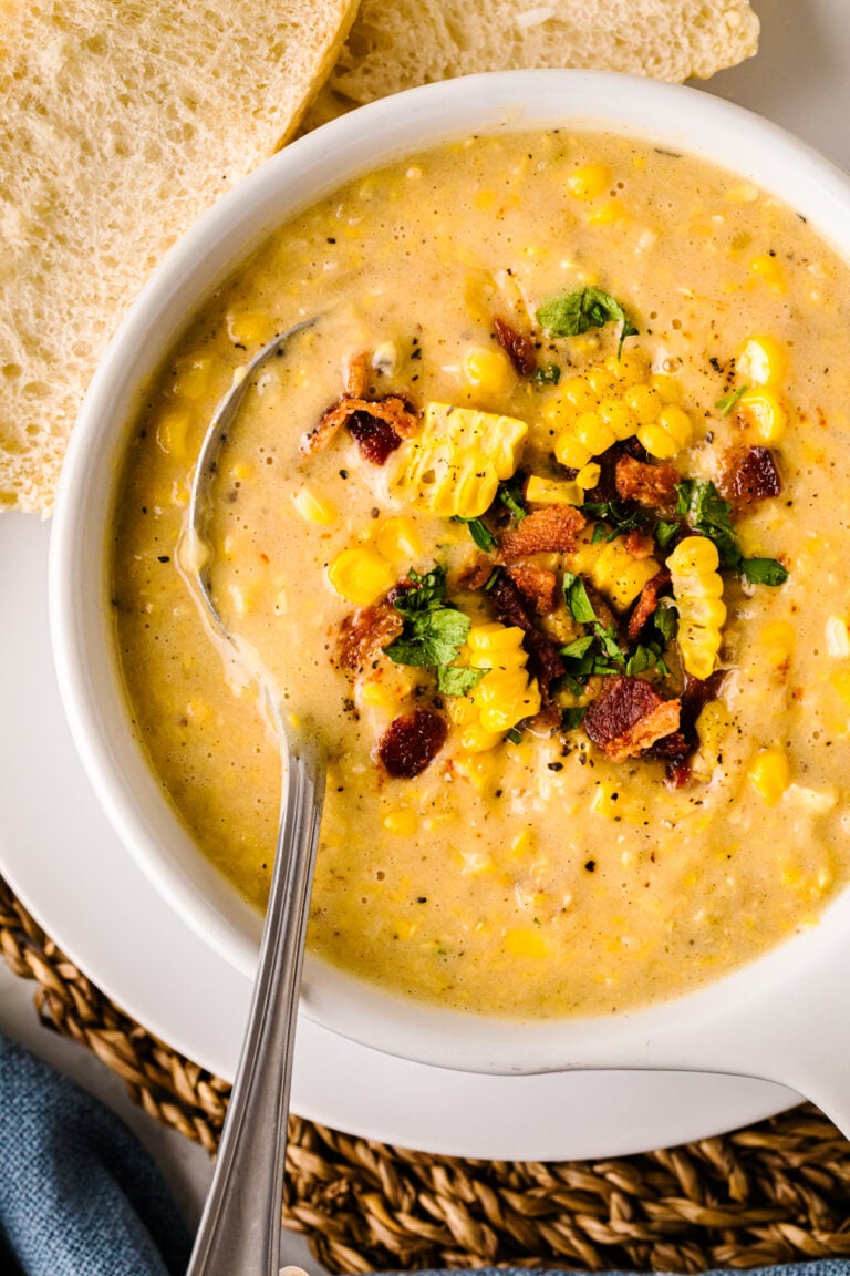 Creamy Corn Chowder in white bowl topped with bacon, corn, cilantro, and black pepper, served with bread slices