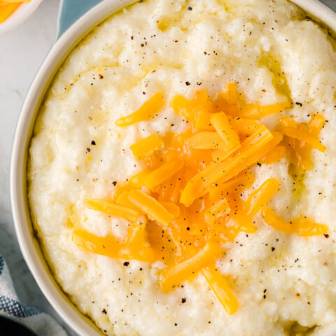Slow Cooker Cheese Grits topped with sautéed yellow peppers and black pepper in a blue and white bowl