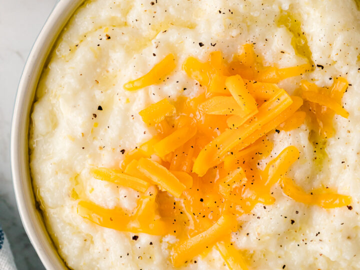 Slow Cooker Cheese Grits topped with sautéed yellow peppers and black pepper in a blue and white bowl