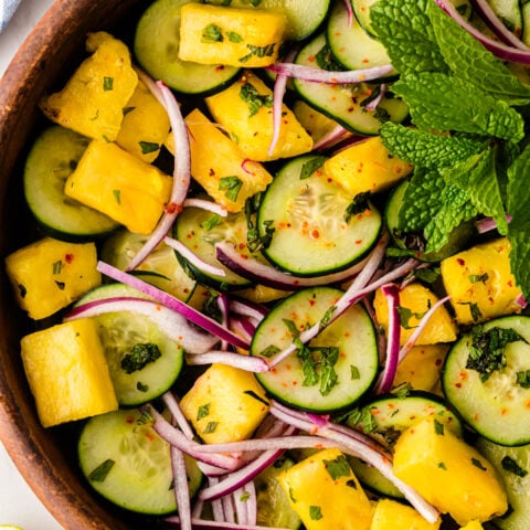 Pineapple Cucumber Salad in wooden bowl with yellow pineapple chunks, green cucumber slices, red onion, fresh mint, and chili flakes