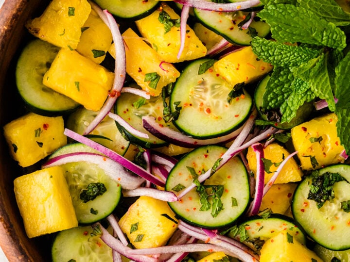 Pineapple Cucumber Salad in wooden bowl with yellow pineapple chunks, green cucumber slices, red onion, fresh mint, and chili flakes